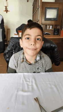 a young boy sitting at a table with a tv on the wall