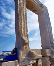 a woman in a blue dress sits under a stone arch