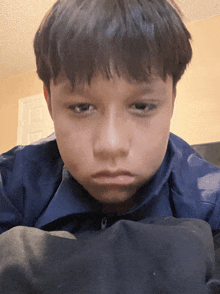 a young boy in a blue jacket looks at the camera with a sad look on his face