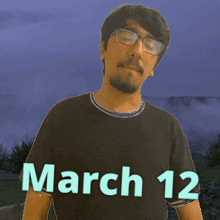 a man wearing glasses and a black shirt that says march 12 on it