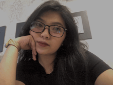 a woman wearing glasses and a watch holds her hand to her face