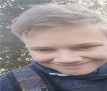 a young boy wearing a blue shirt and a black backpack smiles for the camera