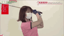 a woman wearing a face mask is holding a golf club in front of a sign that says ngt 48