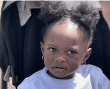 a little girl is sitting in a stroller wearing a white shirt and earrings .