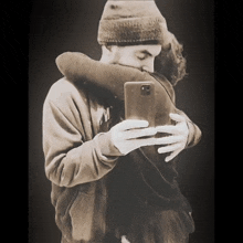 a man in a beanie is hugging a woman while taking a selfie