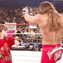 a wrestler is standing in a wrestling ring with a little girl holding a sign in front of a crowd .