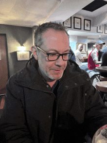 a man wearing glasses and a black jacket sits at a table