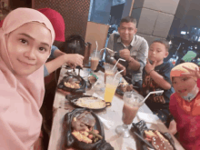 a woman in a pink hijab sits at a table with a man and two children eating food