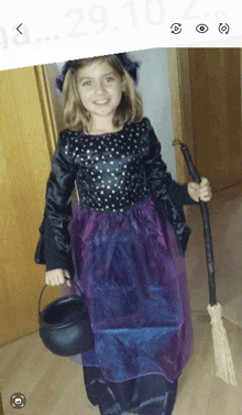 a little girl dressed in a witch costume holds a cauldron and broom