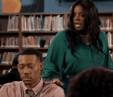 a woman in a green shirt is talking to a man in a pink shirt in a library .