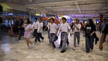 a group of people in white shirts are dancing in a hallway with a sign that says ' a ' on it