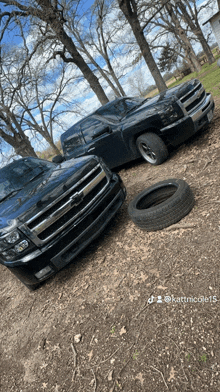 two black chevy trucks are parked next to each other with a tire on the ground