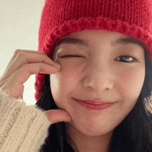 a woman wearing a red hat and a white sweater winks