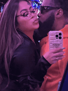 a man kisses a woman while taking a selfie with a prada phone case