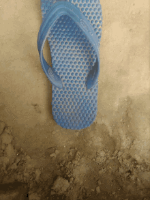 a pair of blue flip flops with holes in them sits on a dirt surface