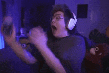 a man wearing headphones and glasses is playing a video game with his mouth open .