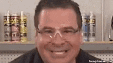 a man wearing glasses and a black shirt is smiling in front of a shelf with bottles of spray paint