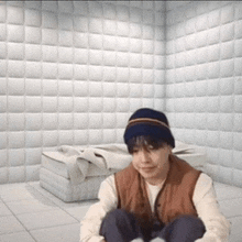 a man wearing a beanie is sitting on the floor in a room with white walls .