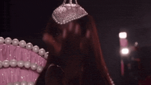 a woman is sitting on a pink couch with pearls and a tiara on her head .