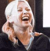 a woman with blonde hair is laughing with her eyes closed and her mouth open .