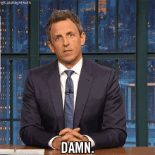 a man in a suit and tie is sitting at a table and says damn