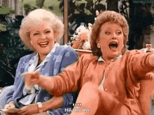 two women are sitting next to each other laughing and pointing at something .