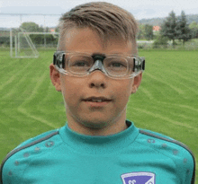 a young boy wearing glasses and a soccer jersey is standing on a field .