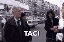 a group of people are standing on a street and the word taci is on the bottom right