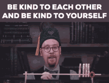 a man wearing glasses and a green hat says be kind to each other