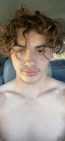 a shirtless young man with curly hair is sitting in the back seat of a car