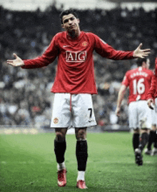 a soccer player wearing a red aig jersey stands on the field with his arms outstretched