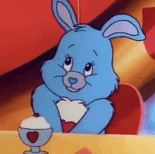 a blue care bear is sitting at a table with a cup of ice cream and a heart on it .