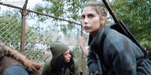 two women are standing next to each other in front of a chain link fence . one of the women is holding a gun .