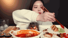 a woman eating a meal with chopsticks and a bowl of food that says ' tasty ' on the bottom