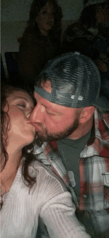 a man and a woman are kissing and the man is wearing a trucker hat