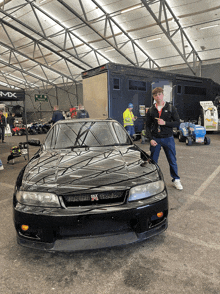 a man stands in front of a black car with the word mx on the side