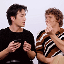 two men sitting next to each other one holding a phone