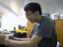 a man wearing glasses is sitting at a table in a kitchen with a bottle of sprite on the counter