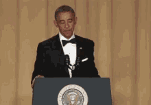 a man in a tuxedo is standing at a podium with the seal of the president of the united states on it