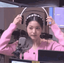 a woman in a pink sweater is wearing headphones and a headband in front of a microphone .