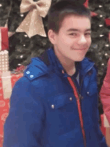 a boy in a blue jacket is smiling in front of a christmas tree .