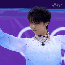 a man in a blue and white outfit is standing in front of a purple background with the olympic rings