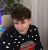 a man wearing a christmas sweater is sitting in a chair and smiling .