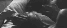 a black and white photo of a man and a woman kissing in bed .