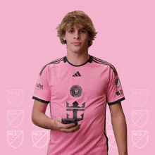 a man in a pink adidas jersey holds a phone