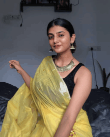 a woman wearing a black tank top and a yellow saree is sitting on a bed