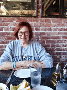 a woman wearing a columbia sweatshirt sits at a restaurant table