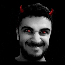 a man with a beard and red eyes is wearing devil horns and smiling .