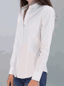 a woman wearing a white shirt and blue jeans is standing in front of a wall .