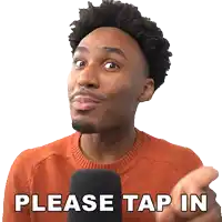 a man wearing an orange sweater is pointing at a microphone and says please tap in